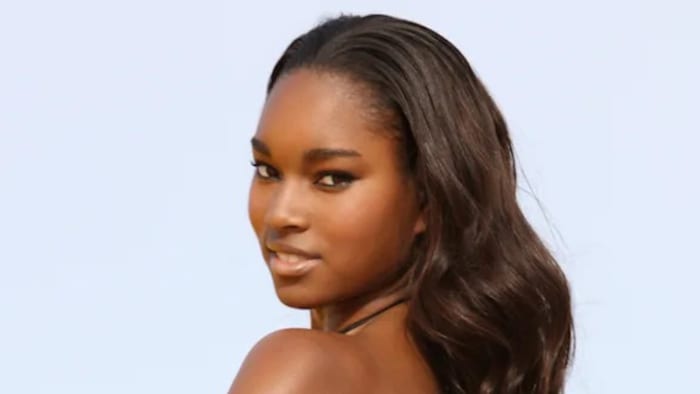 Damaris Lewis poses with her hair in a soft wave and smiles over her shoulder.